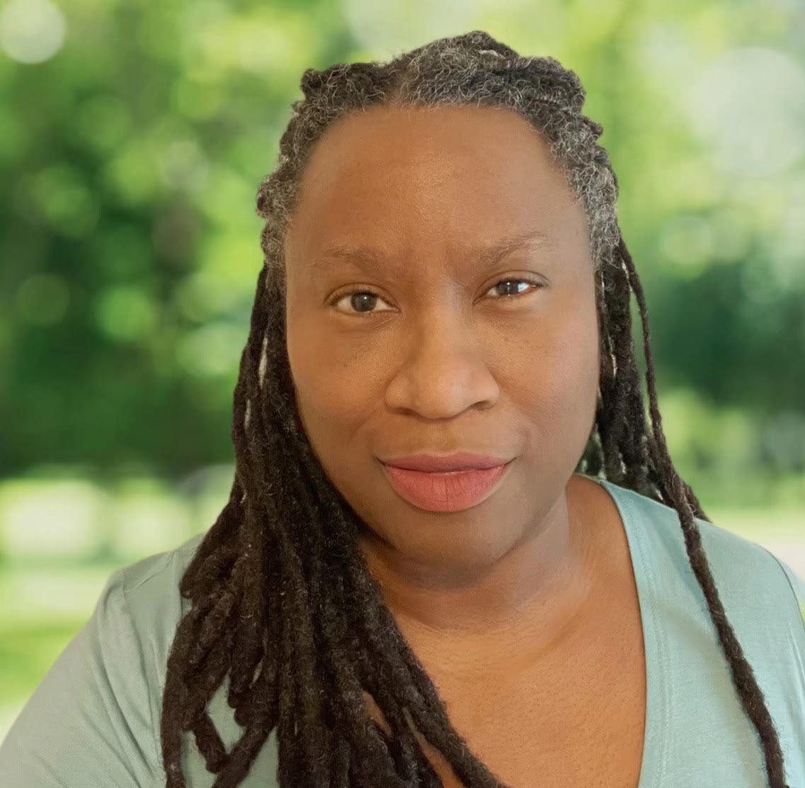 Maya Jewell, a Black woman with braids, wearing a light mint green top with trees and greenery in the background.